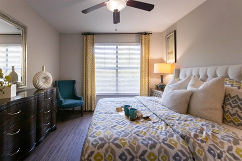 A bedroom with a bed, nightstand, and a ceiling fan in the 826 square foot 1 bedroom, 1 bathroom apartment at The Brownstones Townhome Apartments in the Far North Dallas neighborhood of Dallas, TX.