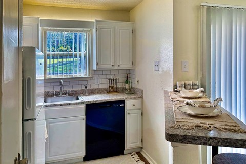 Kitchen in an Efficiency apartment at Cambridge Court Apartments in Dallas, Texas, featuring white cabinetry, range, sink, counter space, and a window.