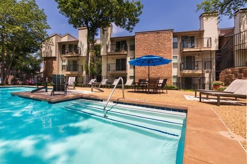 A swimming pool in front of apartment buildings at Canyon Creek Apartments in the Dallas Midtown neighborhood of Dallas, TX.