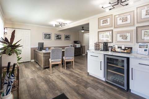 Wide view of the Colonial Ridge leasing office showing the front desk, beverage station, guest seating, framed decor, and wood-style flooring.