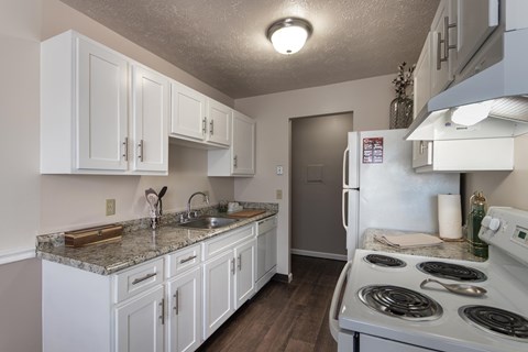 Kitchen at Fairfield Pointe Apartments with white cabinetry, electric range, refrigerator, sink, laminate countertops, and wood-style flooring.