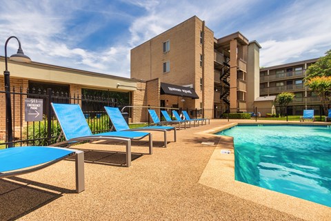 Pool deck with blue lounge chairs and apartment buildings at Harvard Square Apartments in Dallas