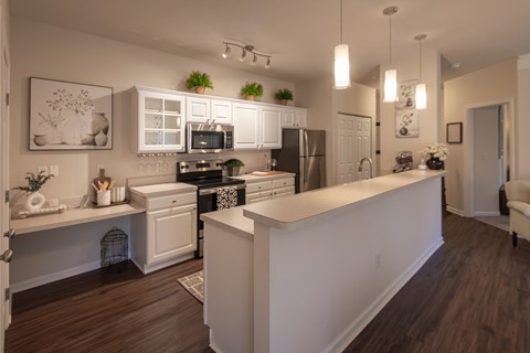 The Islander kitchen opens to the living area through a long breakfast bar, with white cabinetry, dark appliances, and wood-style flooring.