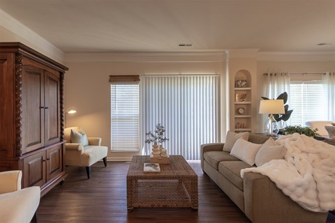 Staged living room at Nantucket Apartments with a sofa, wicker coffee table, entertainment cabinet, and natural light from the adjoining windows.