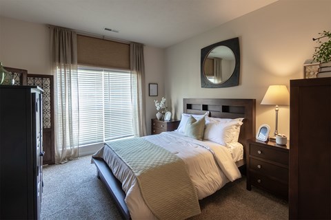 Primary Bedroom in the Islander apartment at Nantucket, with a wood bed frame, matching dressers, carpeted flooring, and a large window with curtains.