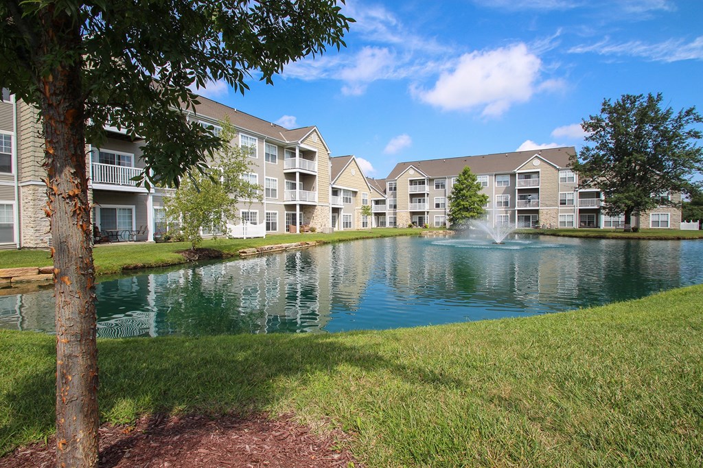 This is a picture of a fountain in a pond with building exteriors at Nantucket Apartments, in Loveland, OH.