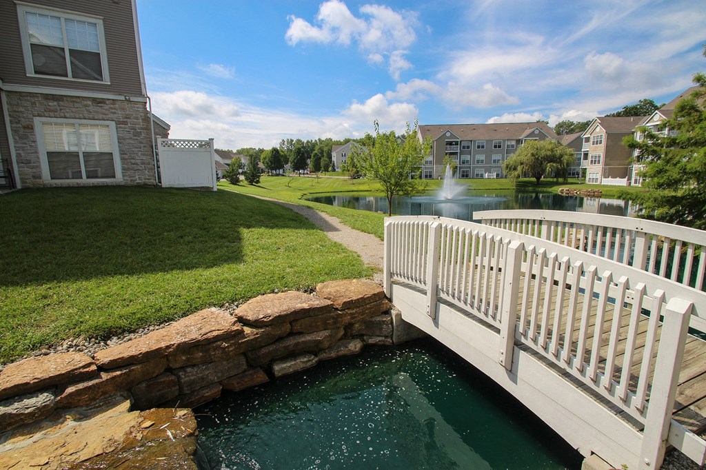 This is a picture of a bridge, pond with a fountain and  building exteriors at Nantucket Apartments, in Loveland, OH.