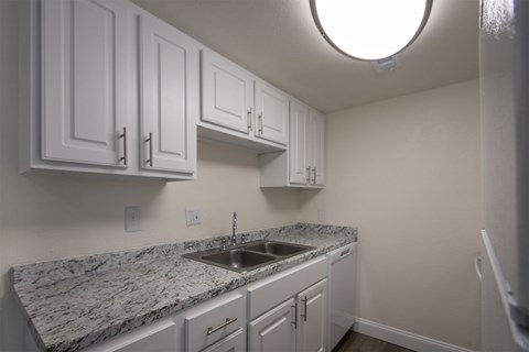 A kitchen with white cabinets and a marble countertop.