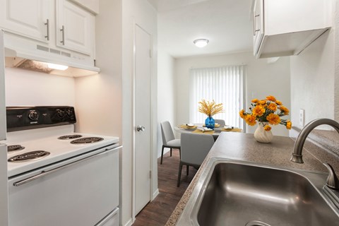 A kitchen with a stove, sink, and a dining table with chairs.