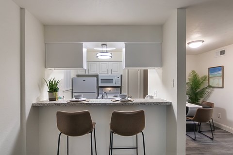 A kitchen with a counter and two chairs.