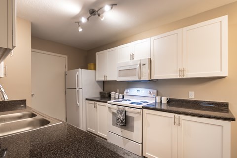 Kitchen appliance wall in the Liberty 2-bedroom apartment, with white cabinets, electric range, refrigerator, microwave, and black countertop.