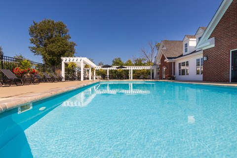 A swimming pool in front of a house with a white pergola.