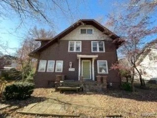 A brown house with a white door and windows is surrounded by trees.