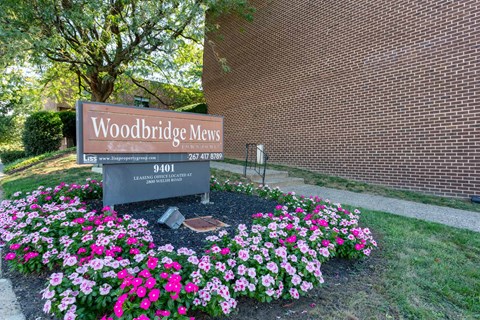 A sign for Woodbridge Mews is surrounded by flowers.