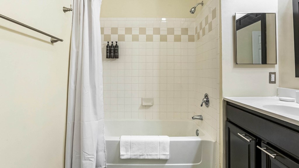 A bathroom with a white tub, black cabinetry, and a shower with a white curtain.at Riverview Landing @ Valley Forge, Eagleville, PA