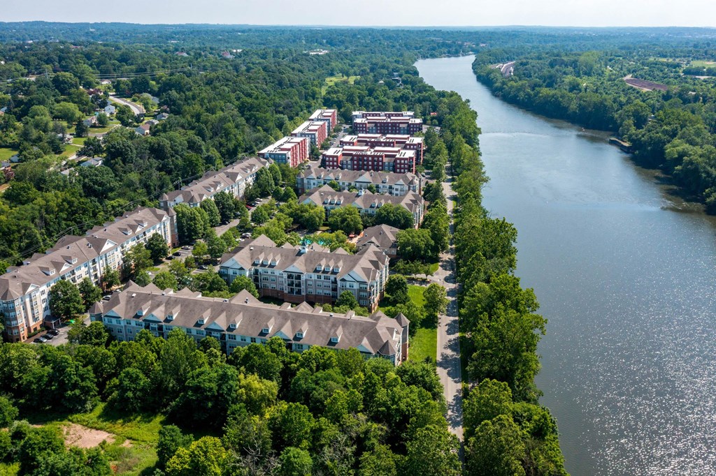 A river flows through a city with apartment buildings on the left and a forest on the right.at Riverview Landing @ Valley Forge, Eagleville, 19403
