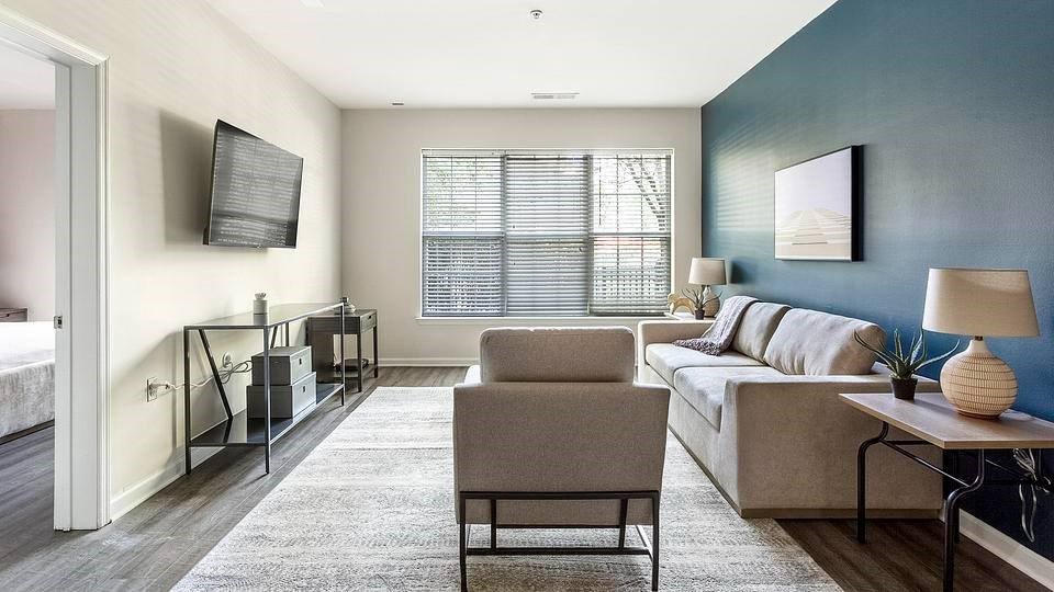 A living room with a grey couch, a chair, a small table, and a television on the wall.at Riverview Landing @ Valley Forge, Pennsylvania, 19403