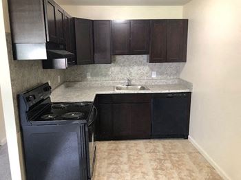 an empty kitchen with black appliances and dark cabinets at Manchester Apartments, Philadelphia, PA 19152