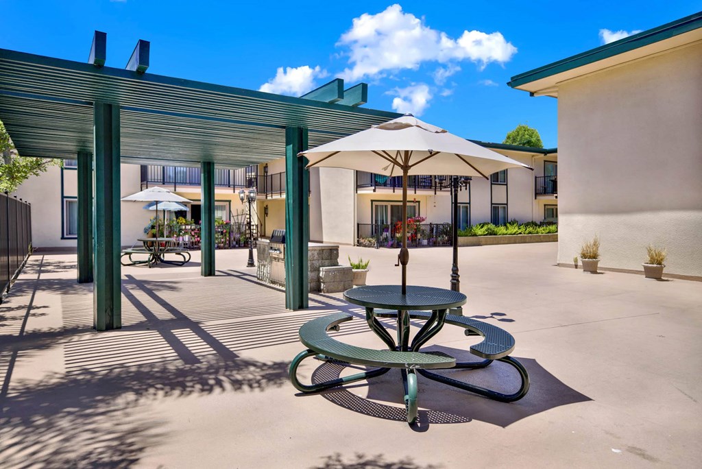 a patio with tables and umbrellas outside of a building at Camino de Oro Apartments, California, 90505