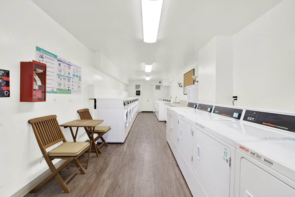 a washer and dryer room in a building with washing machines and two chairs at Camino de Oro Apartments, Torrance, CA