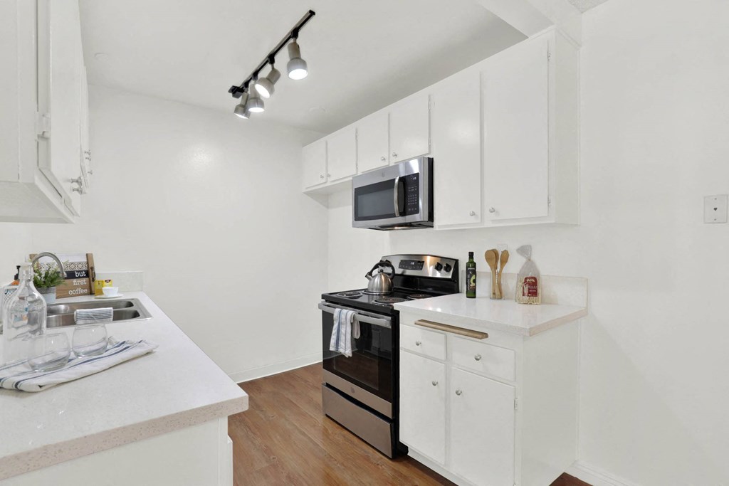 a white kitchen with white cabinets and a black microwave at Camino de Oro Apartments, Torrance, CA
