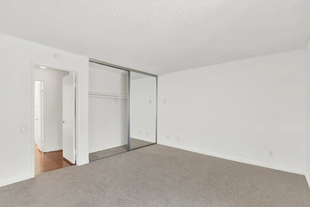an empty living room with white walls and sliding glass doors to a closet at Camino de Oro Apartments, Torrance, California