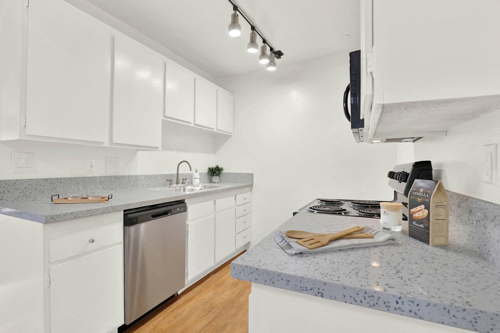 a kitchen with granite counter tops and white cabinets at Camino de Oro Apartments, Torrance, California