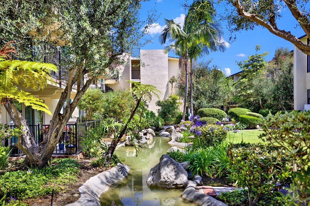 a garden with a pond and palm trees at Willow Tree Apartments, California, 90505