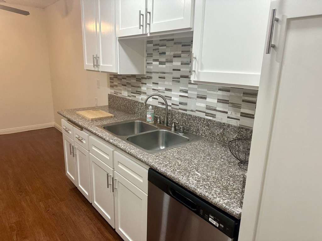 A kitchen with a granite countertop and white cabinets.  at Casa De Oro Apartments, Torrance, 90505