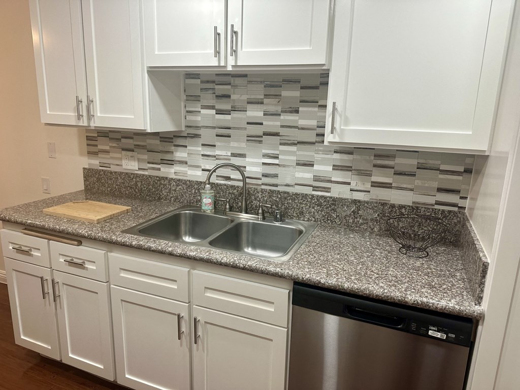 A kitchen with a granite countertop and white cabinets.  at Casa De Oro Apartments, Torrance, 90505