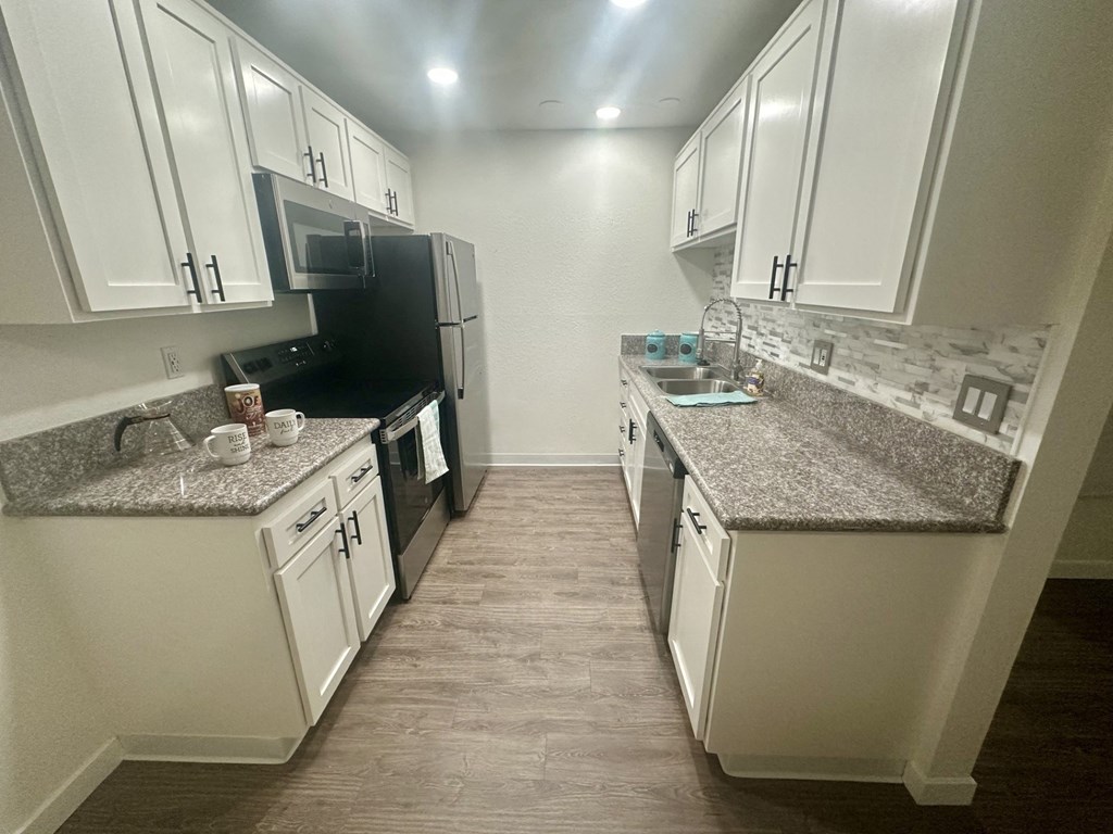 A kitchen with white cabinets and a granite countertop. at Willow Tree Apartments, California, 90505