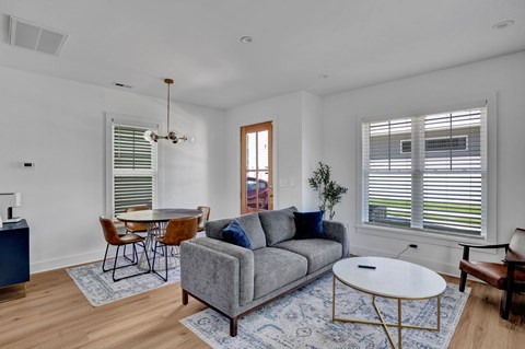 A living room with a grey couch, a white coffee table, and a dining table with chairs.