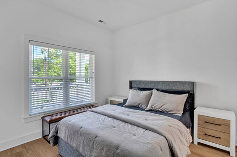 A bedroom with a large bed and a window with blinds.