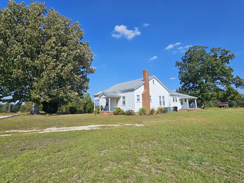 A white house with a brick chimney is surrounded by a grassy field.