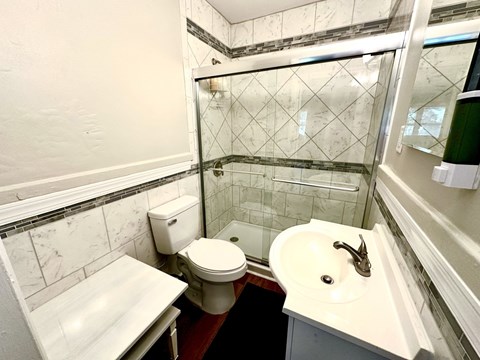 A white toilet sits in a bathroom with a marble tile shower.