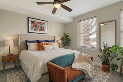 A bedroom with a bed, a ceiling fan, and a potted plant.