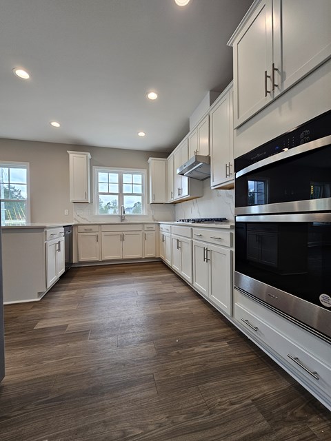 A modern kitchen with white cabinets and a wooden floor.