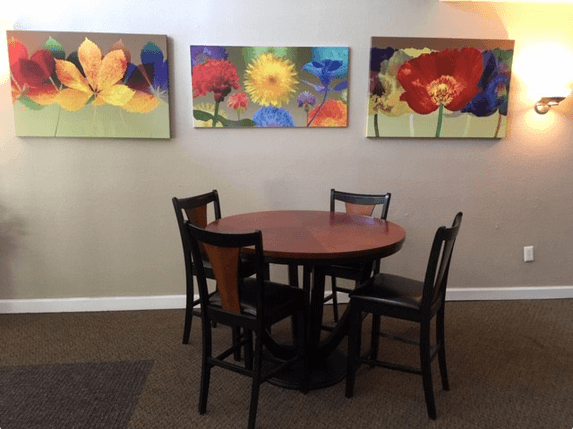 a dining room table with three paintings of flowers on the wall