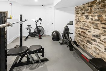 A gym with a rowing machine, a bench, and a wall made of stones.
