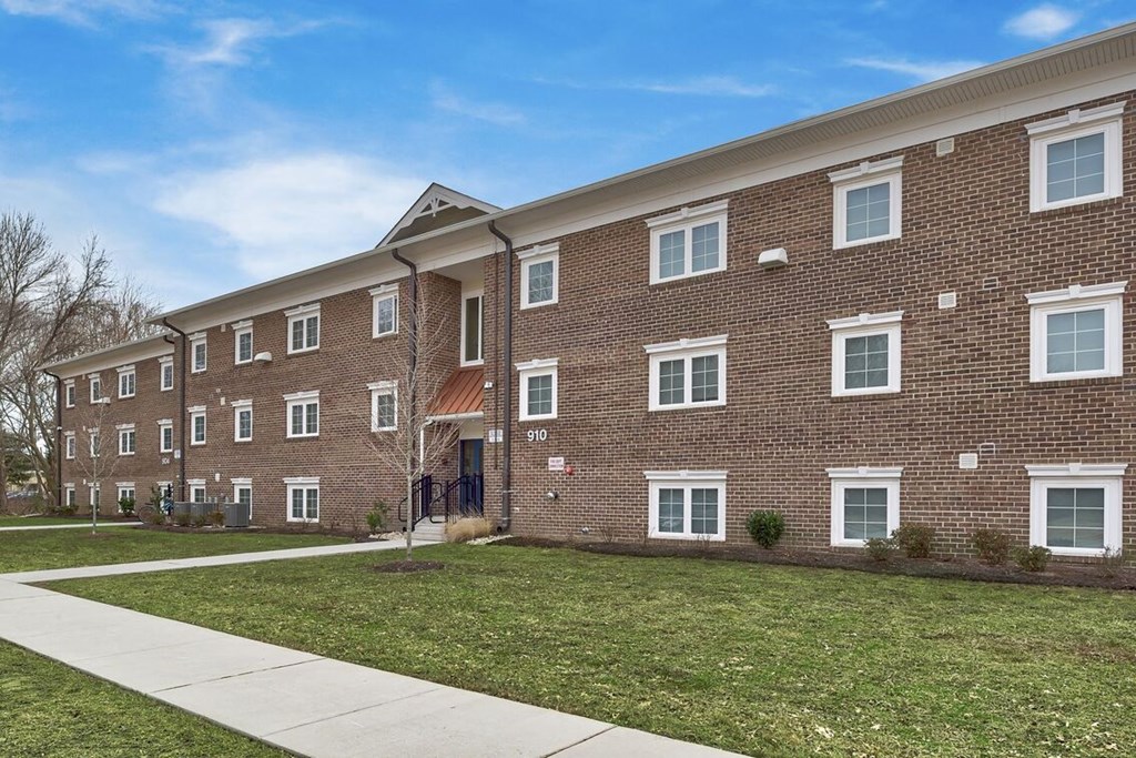 a brick apartment building with green grass and a sidewalk