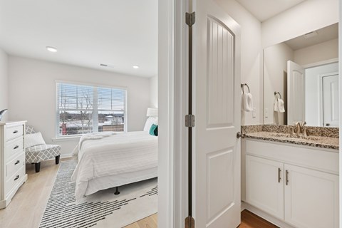 A white bedroom with a large bed and a bathroom with a sink and mirror.