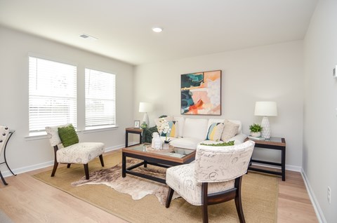 A living room with a white sofa, a chair with a green pillow, and a painting on the wall.
