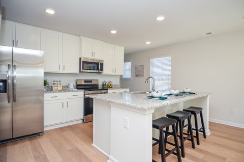 A kitchen with white cabinets and a white island with a bar stool.
