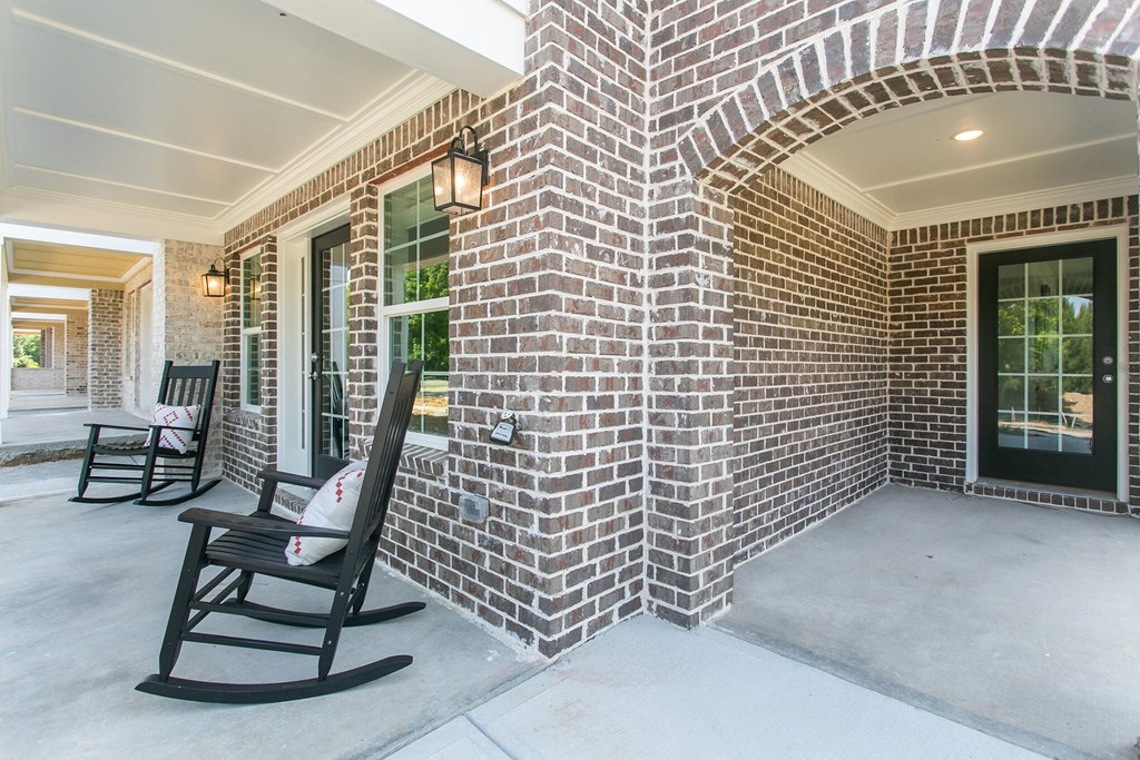 the front porch of a brick house with rocking chairs
