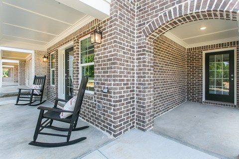 the front porch of a brick house with rocking chairs