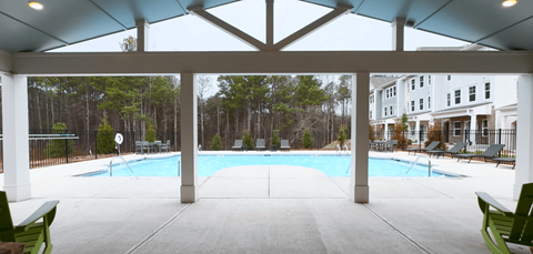 A large covered patio with a pool and green chairs.