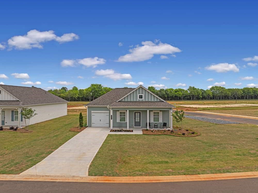 A house with a grey roof and a white garage door is surrounded by a grassy area and a clear blue sky.