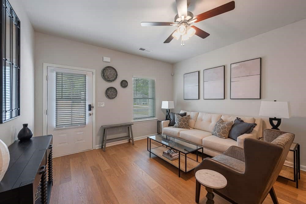 A living room with a white couch, a brown chair, and a ceiling fan.