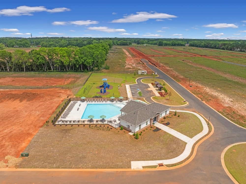 A house with a pool is surrounded by a dirt field.