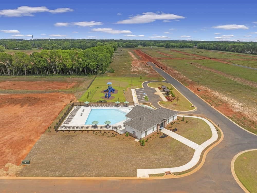 A house with a pool is surrounded by a dirt field.